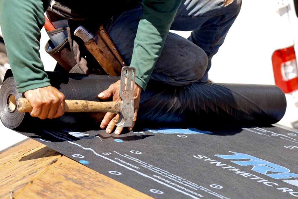 Roofer installing synthetic underlayment on a new shingle roof