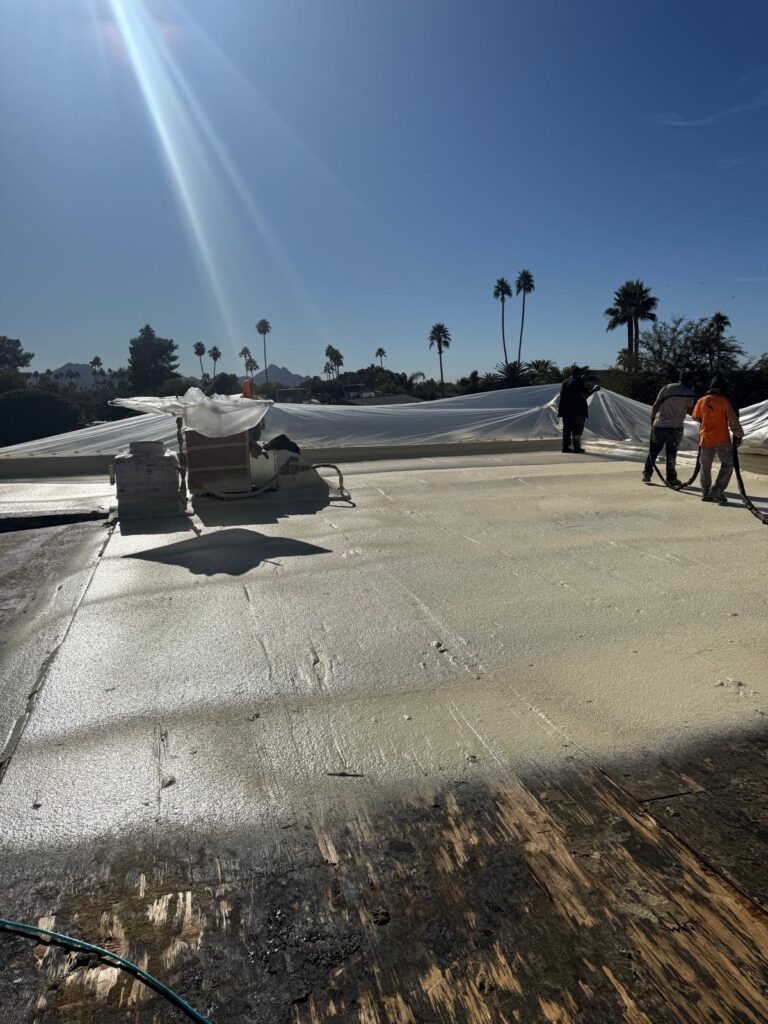 Tip Top Roofing Service crew applying spray foam on a large flat roof