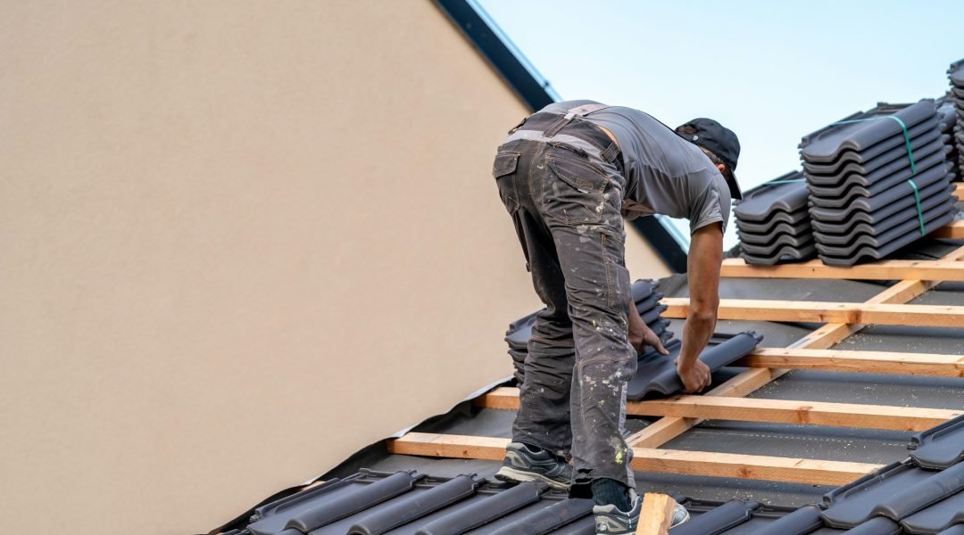 roofer installs a fired ceramic tile on the roof of family house